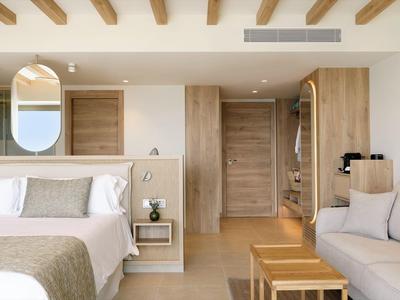 Helles Schlafzimmer mit Doppelbett, Holzdecke, Holztür, Sofa und minimalistischer Einrichtung.