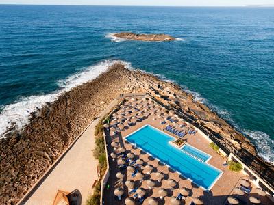 Vista aerea di una piscina con ombrelloni su un'isola rocciosa in mare.