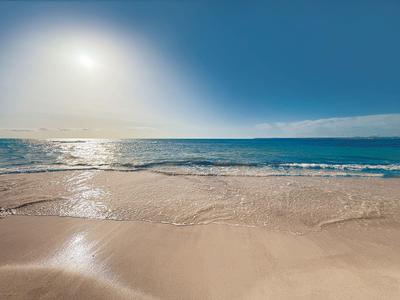 Sunny beach with gentle waves and bright sand under a blue sky.