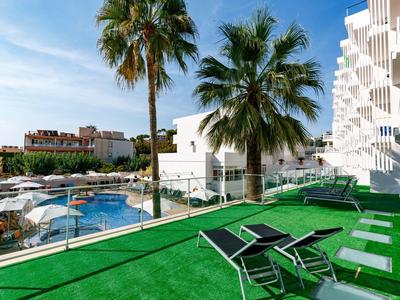 Terrazza dell'hotel con lettini, palme e vista sulla piscina con cielo soleggiato
