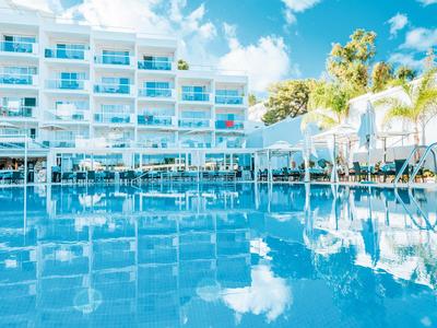 Hotel luminoso con piscina all'aperto, sedie a sdraio e palme sotto un cielo sereno.