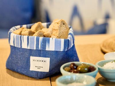 Bread basket with bread pieces on a table, next to bowls of olives and spread.