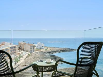 Two chairs and a table on a balcony overlooking the sea and a coastal town.