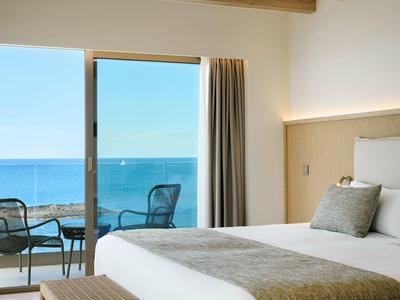 Bright hotel room with sea view, balcony, and two chairs.