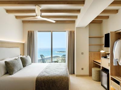 Bright hotel room with double bed, ceiling fan, and sea view from balcony.