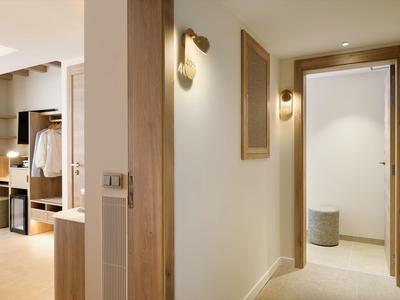 Modern hotel corridor with bright lighting and wooden details on doors and walls.