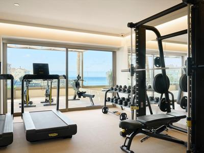 Lichte fitnessruimte met trainingsapparatuur en uitzicht op zee door grote ramen.