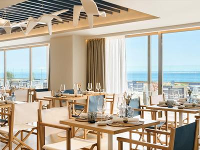 Bright restaurant with wooden furniture and sea view through large windows.