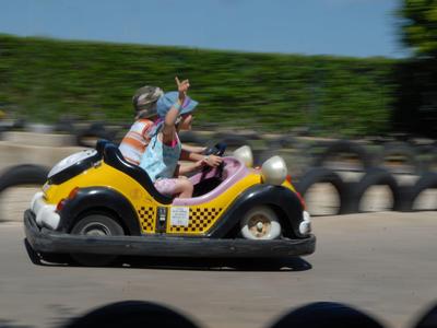 Two people joyfully driving a yellow go-kart on a racetrack outdoors.