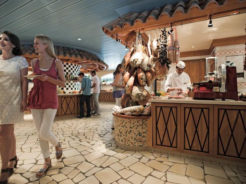 Two women walking in a hotel lobby with a food display and staff in the background.