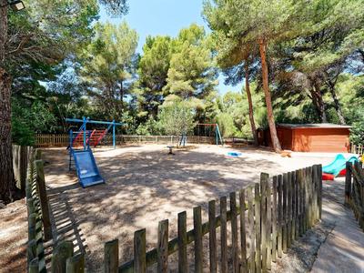 Parco giochi con altalene e sabbia circondato da alberi e recinzione in legno in un parco