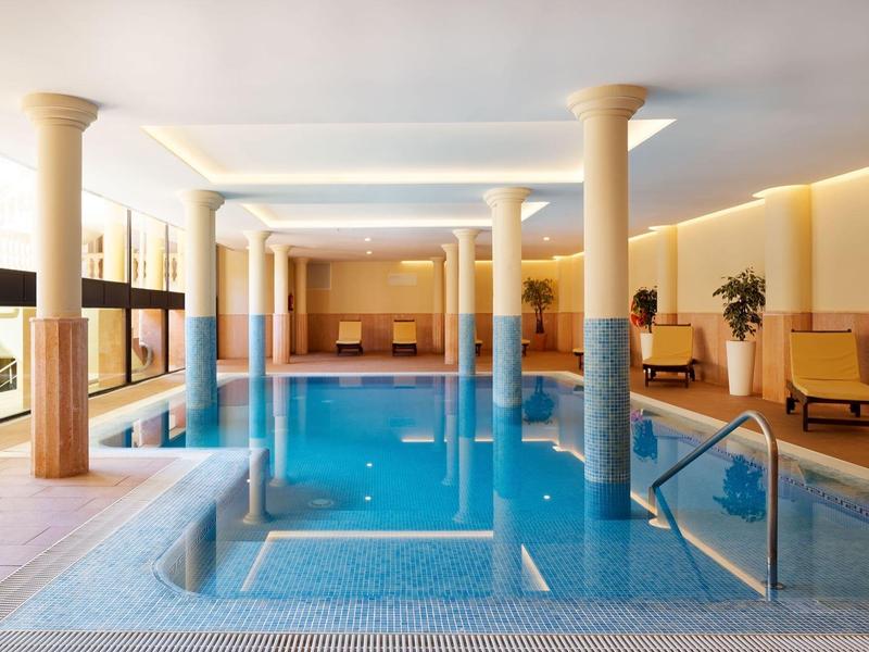 Piscina coperta in una stanza luminosa con colonne e aree salotto