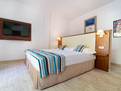 Modern hotel room with double bed, TV, and minimalist decor.