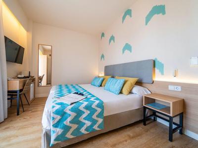 Bright bedroom with double bed, colorful pillows, desk, and wall decoration.