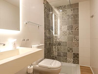 Moderne Badezimmerecke mit beleuchtetem Spiegel, Waschbecken, Toilette und gemusterten Fliesen.