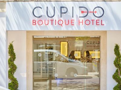 Facade of Cupid Boutique Hotel with glass door and car reflection.