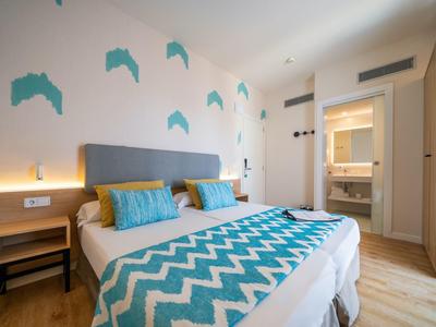 Modern hotel room with double bed, turquoise pillows, and wave-patterned bedspread.