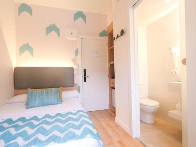 Small hotel room with single bed, blue pillow, wooden floor, and adjoining bathroom.