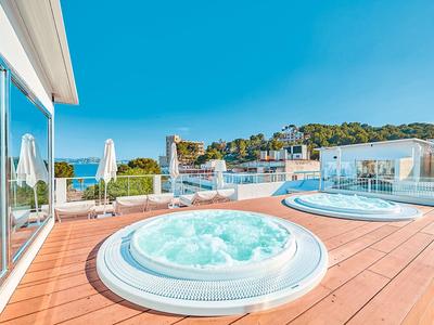 Moderna zona de piscina de hotel con dos jacuzzis y vista al mar en un día soleado.