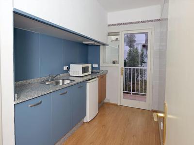 Kleine keuken met blauwe kasten, magnetron, kleine koelkast en toegang tot balkon.