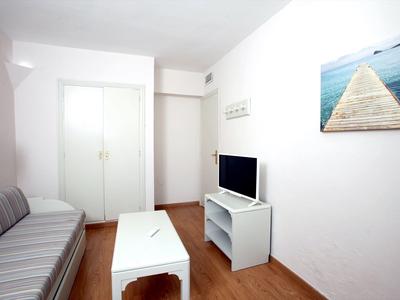 Lichte woonkamer met bank, witte salontafel en tv op een wit meubel.