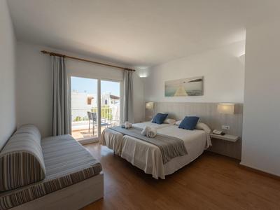 Bright hotel room with double bed, sofa, wooden floor, and balcony overlooking the city.