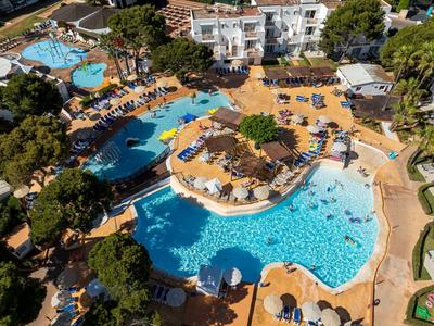 Aerial view of a hotel with multiple pools, sun loungers, and green trees.