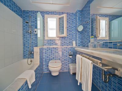 Modern bathroom with blue tiles, bathtub, sink, and toilet beneath a window.