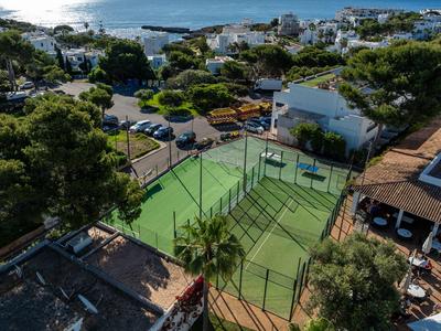Court de tennis dans une zone hôtelière avec bâtiments environnants et mer en arrière-plan