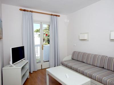Bright living room with gray sofa, white table, and TV in front of balcony door with curtains