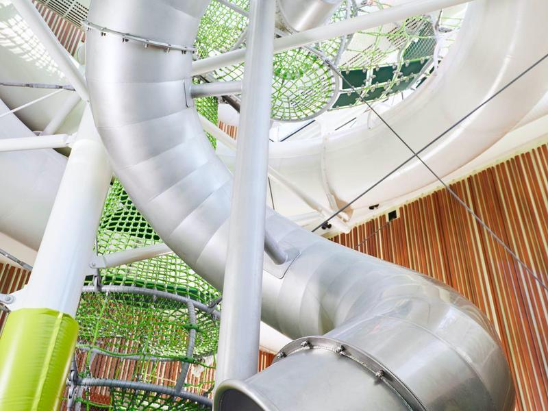 Large indoor silver spiral slide in a modern wooden and glass atrium space.