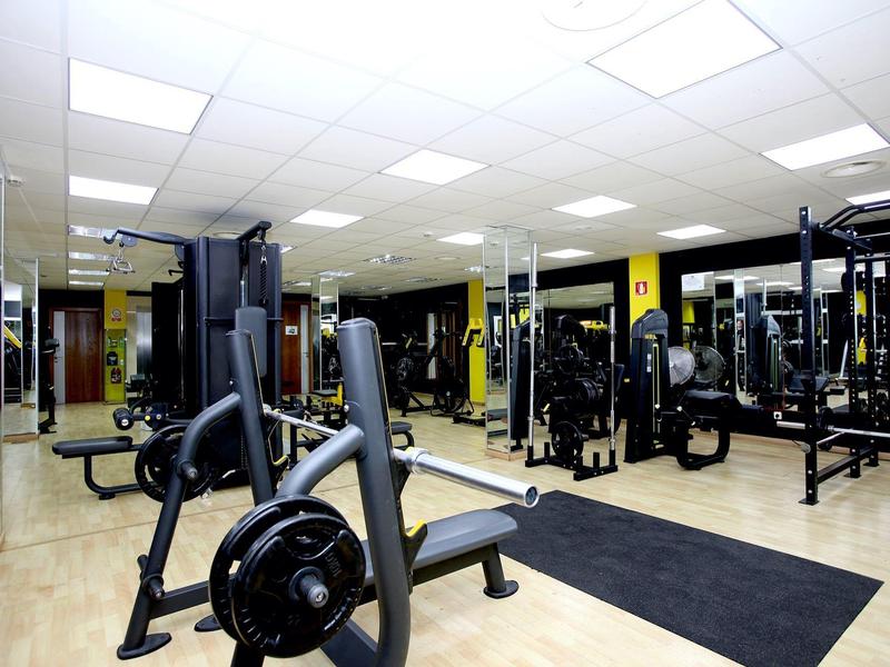 Modern gym with various strength training machines, mirrors, and light flooring.