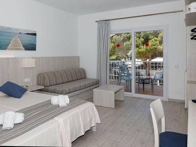 Bright hotel room with two beds, sofa, balcony, and view of green trees.