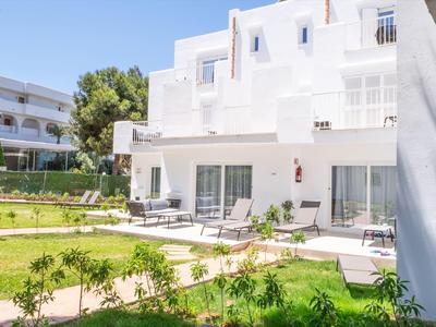 White hotel building with terrace and sun loungers, green garden in the foreground