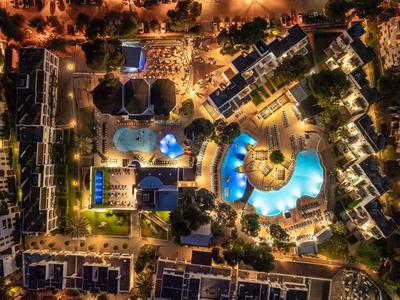 Night view of a resort with illuminated swimming pools and surrounding buildings.