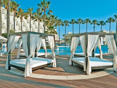 Luxurious white canopy beds by the pool with palm trees and blue sky in the background.