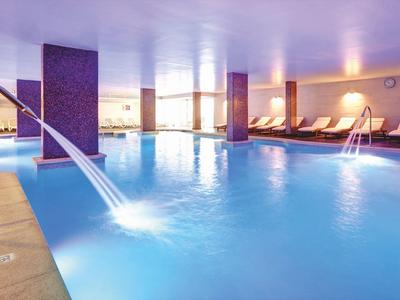 Indoor pool with waterfall feature and lounge chairs in a bright spa area.