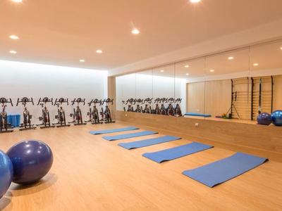 Ein heller Fitnessraum mit blauen Yogamatten, Gymnastikbällen und Spinningrädern an der Seite.