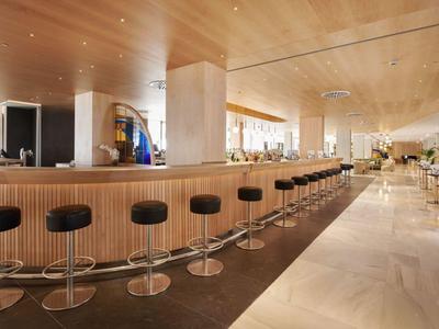 Brede hotelbar met houten panelen en zwarte barkrukken op een rij.