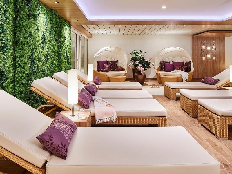 Ontspannen spa lounge met houten ligstoelen, paarse kussens en een groene plantenmuur.