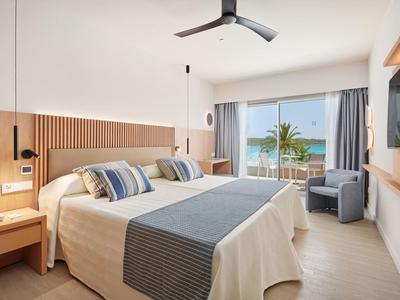 Modernes Hotelzimmer mit Doppelbett, Meerblick und Balkon mit Palmen.