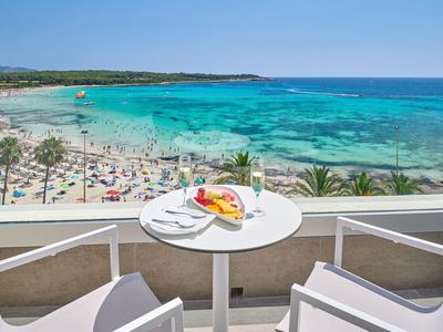 Balkon mit Tisch, Stühlen und Blick auf belebten Strand und türkisfarbenes Meer.