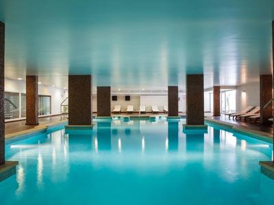 Großer Indoor-Pool mit Säulen und bequemen Liegen im modernen Wellnessbereich.