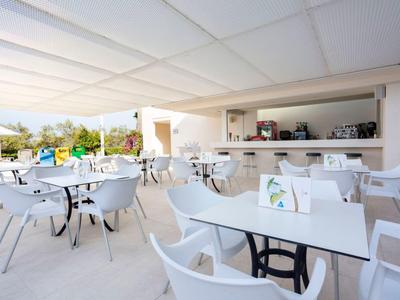 Moderní venkovní terasa restaurace s bílými stolky a židlemi pod střechou.