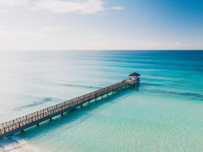 Longue jetée s'étendant sur une mer turquoise jusqu'à une petite cabane sous un ciel clair.