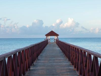 Jetée en bois menant à un pavillon au-dessus de la mer calme sous un ciel bleu.