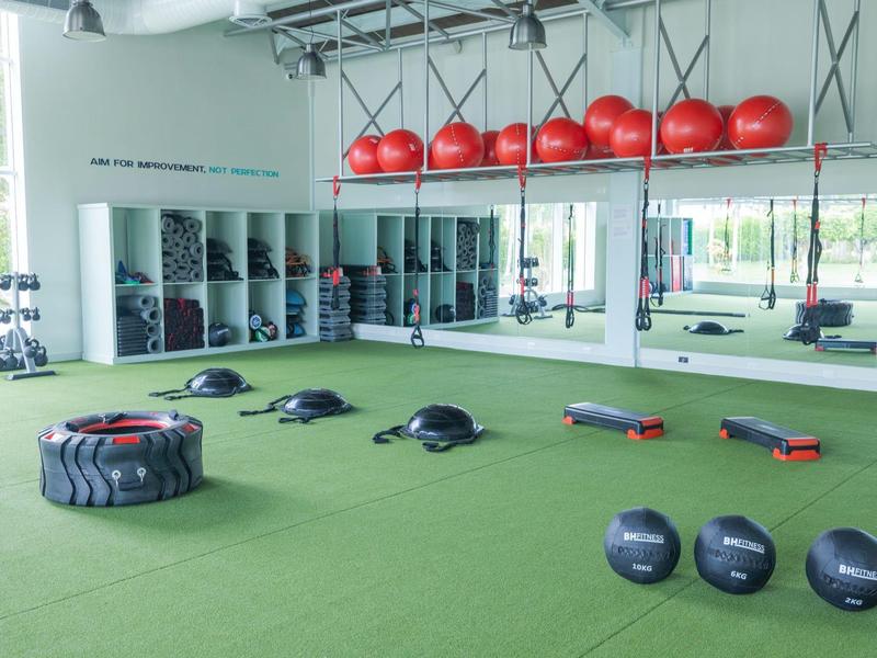 Salle de sport moderne avec tapis vert, ballons rouges, poids et gros pneus.