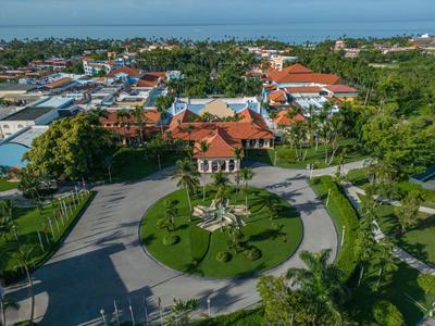Aerial view of a resort with traditional architecture, spacious lawn, and coastal view in the background.