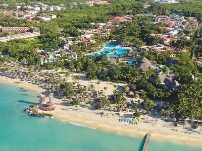 Aerial view of a tropical beach resort with pool and palm trees along the coast.