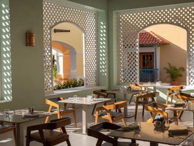 Brightly lit hotel dining area with tables and chairs in an open, architecturally designed space.